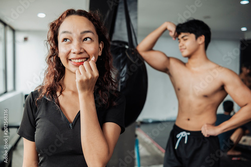 Tableau sur toile Young woman smiles excitedly after noticing a handsome shirtless man flexing con