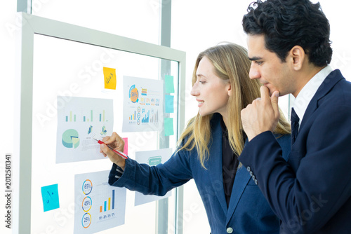Man and woman businesspeople planning business strategy while looking at infographic on wall. Business, education and office concept.