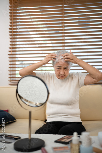 Bilde på lerret Senior woman sitting on couch checking her hairline or grey hairs by looking at mirror in living room at home