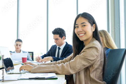 Young cheerful Asian business woman discussing project with colleagues while working together in the modern office.