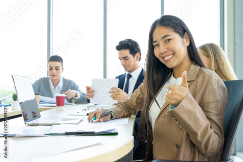 Young cheerful Asian business woman discussing project with colleagues while working together in the modern office.