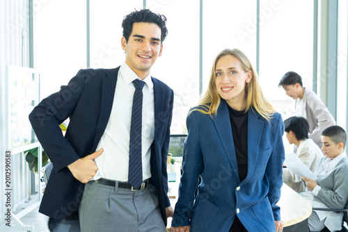 Businesswoman and businessman leader looking at camera in modern office with businesspeople working at the background. Teamwork concept. 