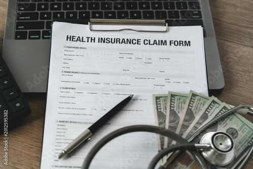 Fotografie Healthcare cost calculator on health insurance claim form with US dollar bills, stethoscope, and pen on laptop, medical financial planning for hospital expenses and policy coverage budget