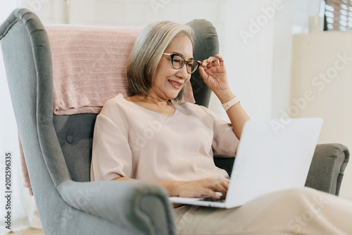 Senior woman using Laptop computer sitting relax calm at home enjoy happy smiling