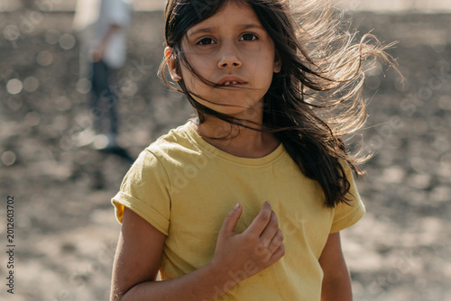 Portrait of thoughtful girl looking at camera close up, indian spanish child in yellow t-shirt, day, nature