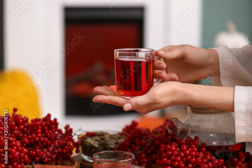 Foto Young woman holding cup of hot viburnum tea at home, closeup