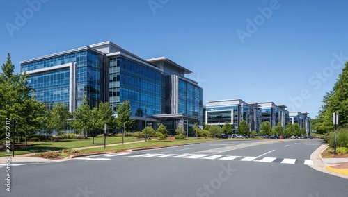 Modern glass office buildings line a tree-lined street under a clear blue sky