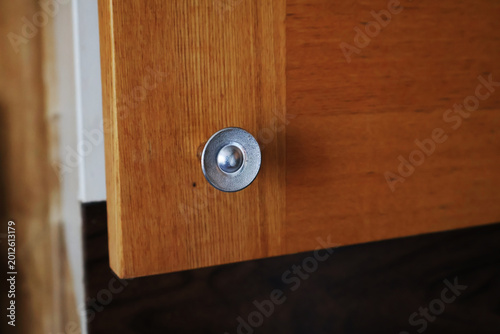 Close-up of sleek metal knob mounted on warm-toned wooden cabinet door. Image conveys simplicity and practicality of everyday design, evoking sense of order and understated elegance. Soft focus backgr