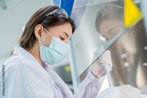 Scientist conducts laboratory experiment with pipette while wearing safety gear in a research facility