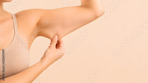 Close-up of woman's hand pinching arm fat, flabby underarm skin tightening and body contouring concept with massive copy space on beige background.