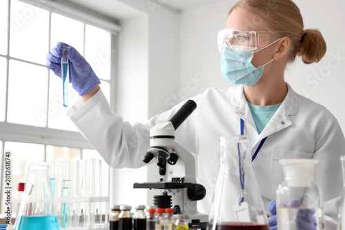 Female scientist with medical mask and test tube working in laboratory