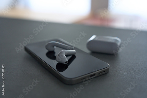 Wireless earphones on smartphone with charging case on dark gray desk