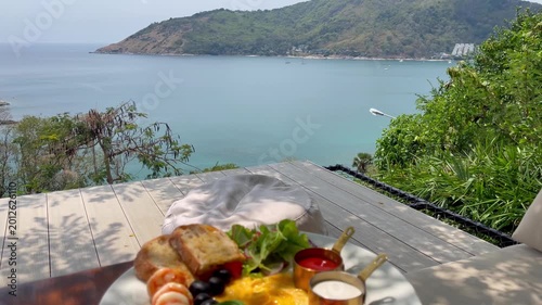Elegant tropical breakfast served overlooking the Andaman Sea in Phuket, featuring fresh bread, smoked salmon, avocado, shrimp, salad, sauces, and panoramic coastal scenery in a luxury vacation spot