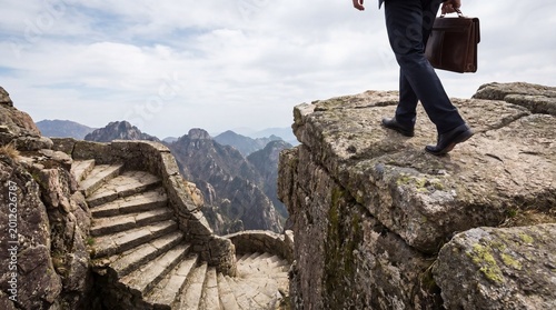 Foto Determined businessman stepping across a treacherous rocky cliff towards uncertain future path