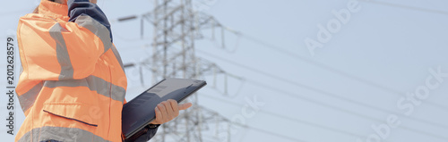 Canvastavla A worker stands outside in bright clothing and looks up at the power lines