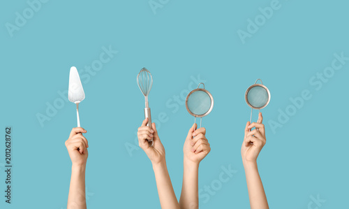 Quadro su tela Female hands holding sieves with cake spatula and whisk on blue background