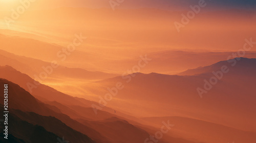 Golden Sunset Over Layered Desert Mountains with Atmospheric Haze and Warm Orange Landscape