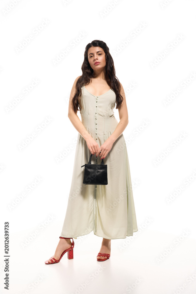 Naklejka premium Stylish young woman poses elegantly in a trendy summer dress on a bright studio backdrop