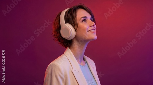 Woman wearing white headphones and smiling while listening to music on a purple background