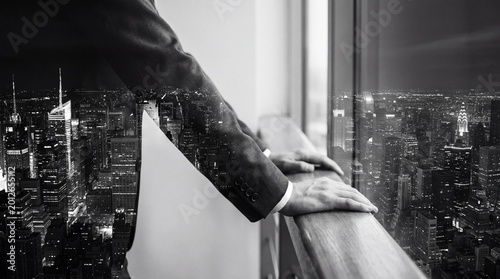 Photography Double exposure in black and white of a businessman's hands on a railing, layered with a sprawling city night panorama