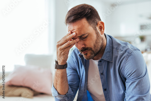 Bild auf Leinwand Stressed Man With Headache Rubbing Forehead While Sitting At Home Looking Tired