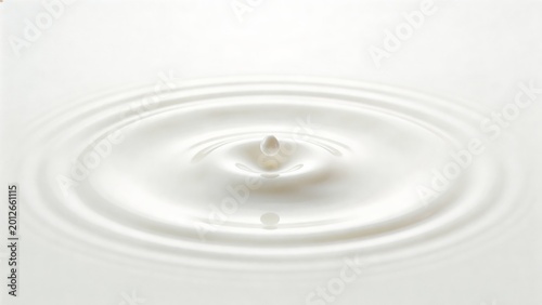 A single drop of cow milk creates ripples on a white surface, highlighting the smooth and creamy texture of the dairy product.