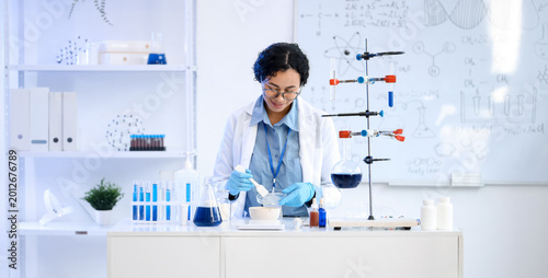 Pretty young African-American female chemist with mortar and Petri dish worki...