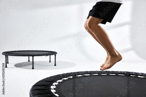 Energetic view of a child’s legs in the air while jumping on a fitness mini trampoline in a bright, modern studio. A concept for active play on International Children's Day.