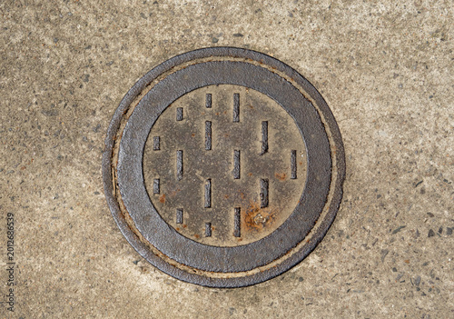 Schilderij op canvas Top-down view of a weathered circular iron manhole cover with rhythmic geometric patterns and rust textures