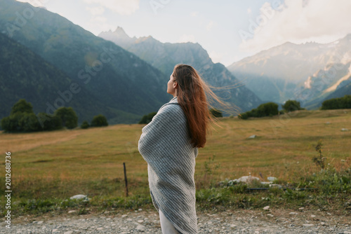 Cuadro en lienzo Young woman wrapped in a gray shawl stands in a windswept meadow, looking toward