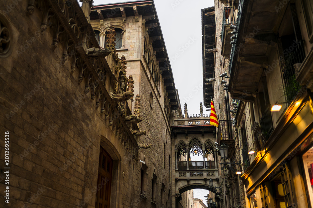 Fototapeta premium Historic Gothic bridge and narrow street in Barcelona Spain with Catalan flag creating authentic old town atmosphere and cultural travel destination