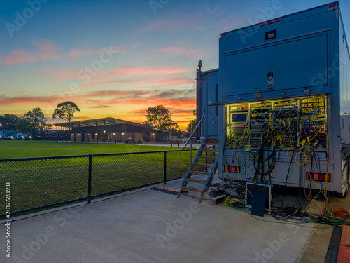 Fotografi Outside broadcast truck with complex wiring and equipment at a sports stadium during sunset