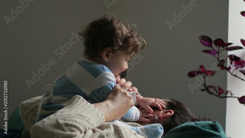 Foto Mother lying on sofa holding baby above her, infant looking at parent with curio