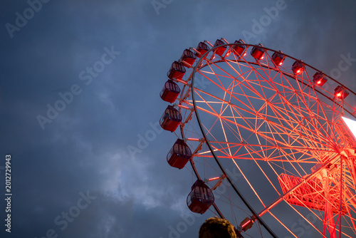 Illuminated Red Ferris Wheel Against a Dark Cloudy Night Sky