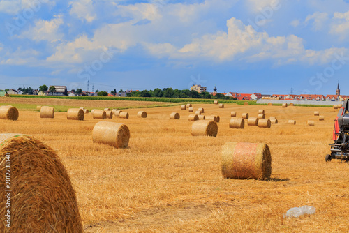 Foto Bales of hay on a farm field with a tractor under a clear blue sky during the su