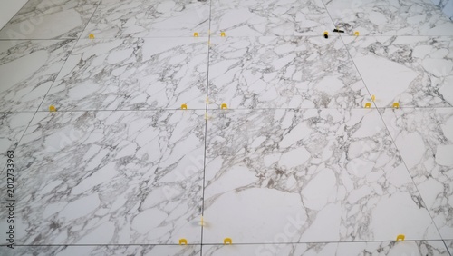 Close up view of freshly laid marble effect porcelain floor tiles. Yellow spacers and leveling system are in place during installation. Renovation and construction concept for home improvement