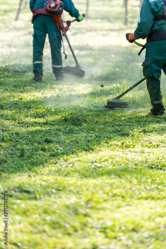Two Groundskeepers Cutting Grass in Sunny Park