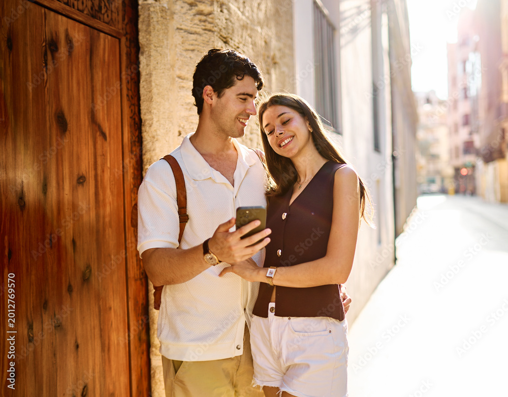 Naklejka premium Couple enjoys a sunny day walking together in a charming urban area during late afternoon or tourists visiting a destination looking at phone map app