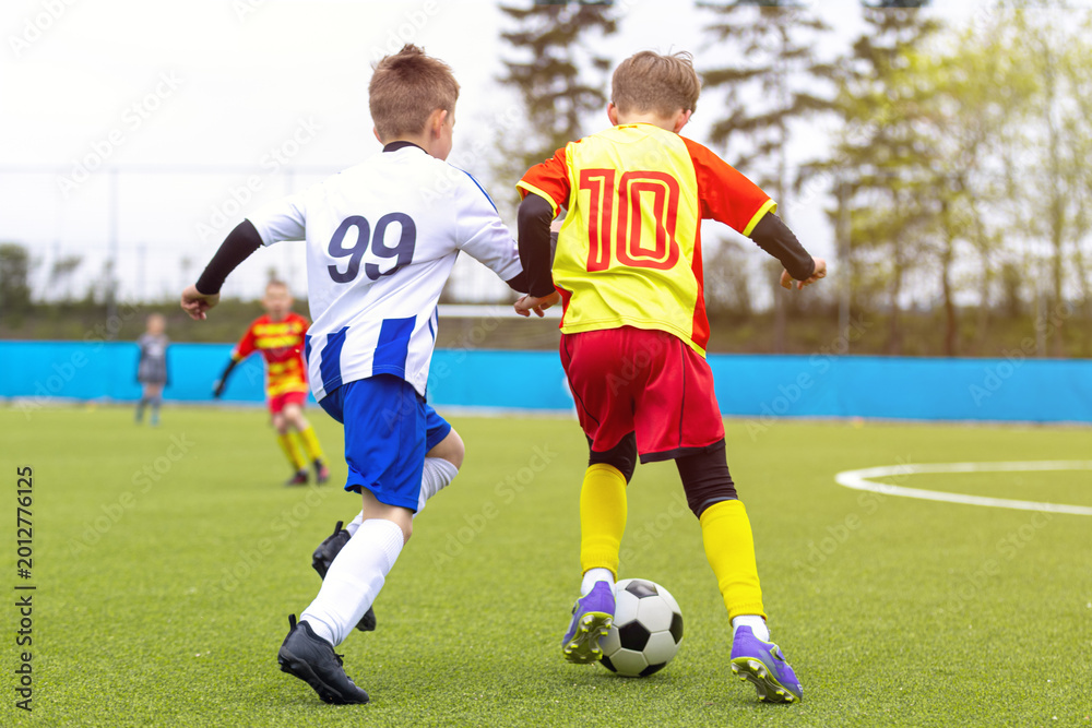 Fototapeta premium Junior Soccer Players in Blue and Yellow Kits Competing for Ball Possession During League Match - Youth Football Duel Between Number 99 and Number 10 on Turf