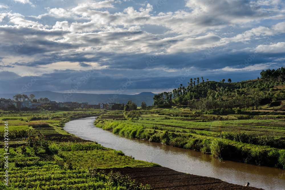 Fototapeta premium Winding river flows through lush agricultural fields near Antsirabe