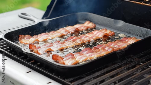 Crispy Bacon Sizzling on a Cast Iron Skillet on a Grill.