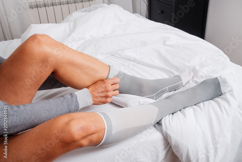 Canvas Print a man adjusts compression socks on a bed