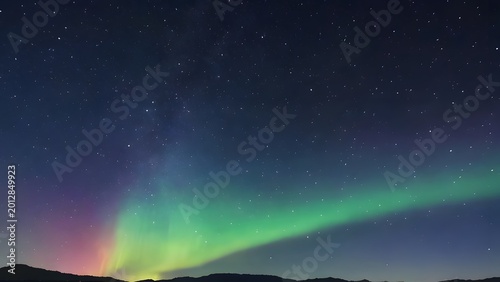 Aurora Borealis dancing above a dark landscape at night with starry sky and subtle horizon glow