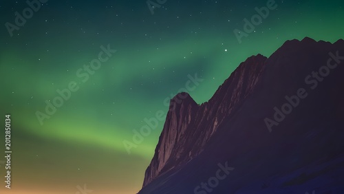 Aurora Borealis over rugged mountain peak during twilight with starry sky