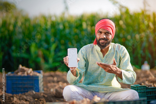 young indian farmer sitting at turmeric farm showing smartphone screen