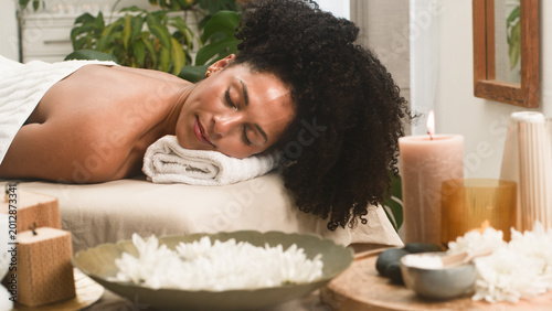 Relaxed Woman Receiving Spa Massage Surrounded by Candles and Flowers in Tranquil Treatment Room