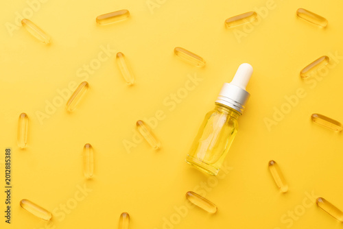 Obraz na płótnie Oil capsules and serum bottle with dropper on yellow background