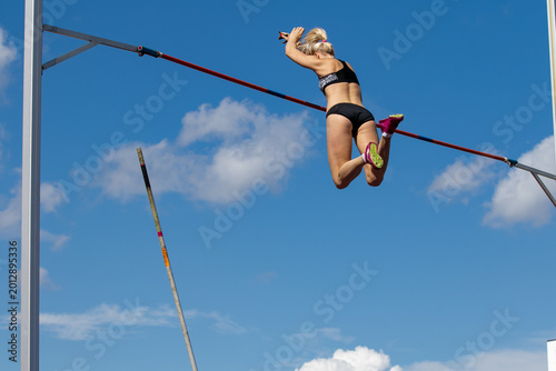 Female athlete flying on background blue sky in pole vault