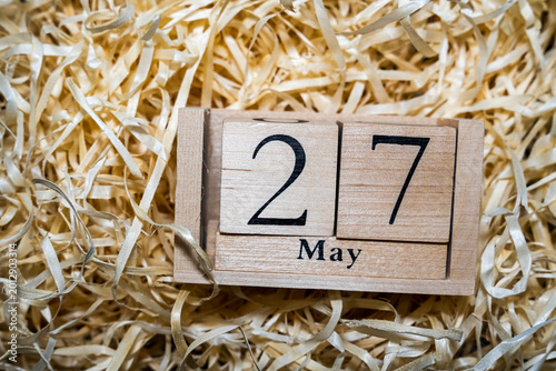 A wooden calendar displaying the date 27 May, surrounded by shredded paper, ideal for themes of time management and planning.