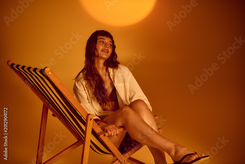 Vibrant young woman enjoys summer vibes while relaxing in a stylish chair under warm sunlight